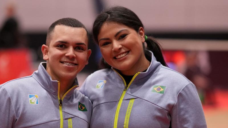 A male athlete and a female athlete pose for a photo together. They are wearing Brazil's gray jersey
