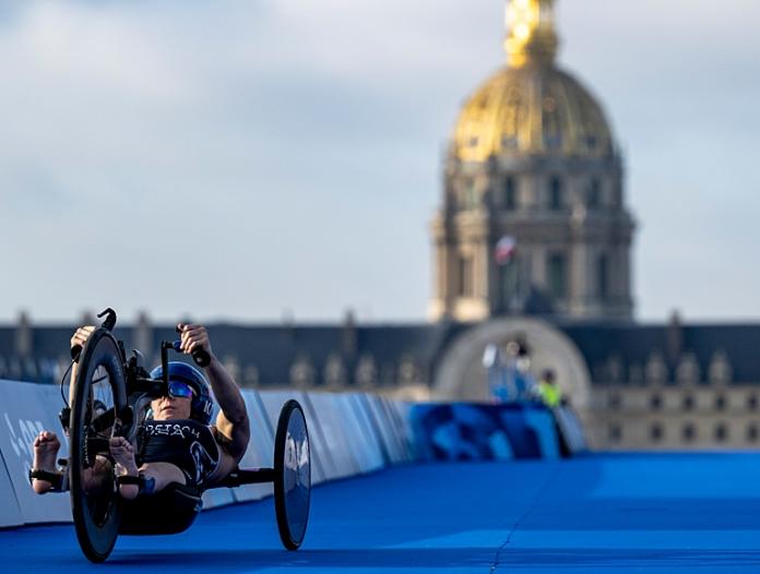 A female Para triathlon athlete is competing in a handcycle at Paris 2024. 