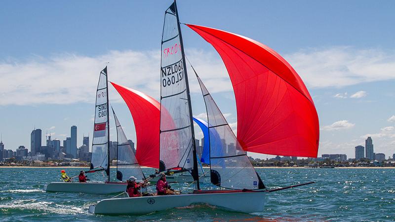Two boats with red sails on the water in front of a skyline