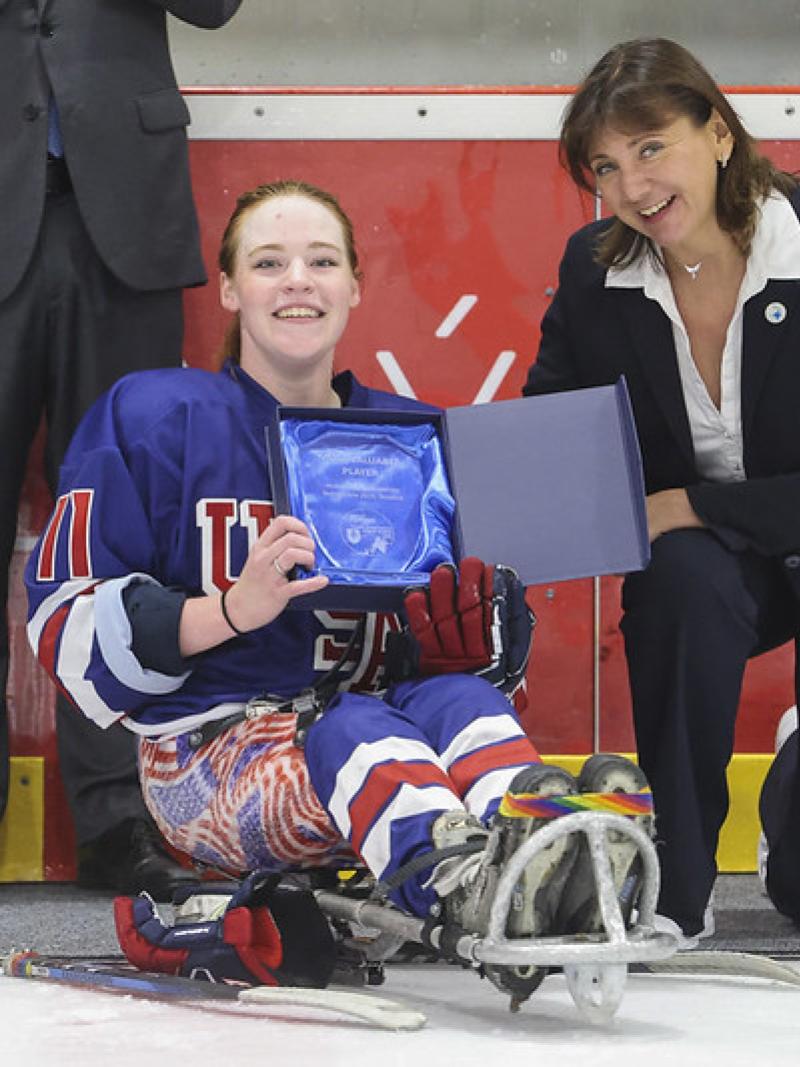 A female Para ice hockey player receiving an award next to a woman on the ice