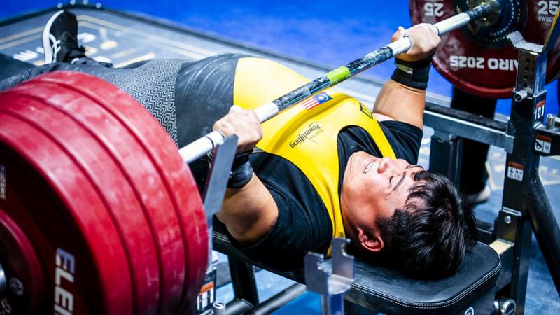 A short stature man lifting weight in a Para powerlifting competition