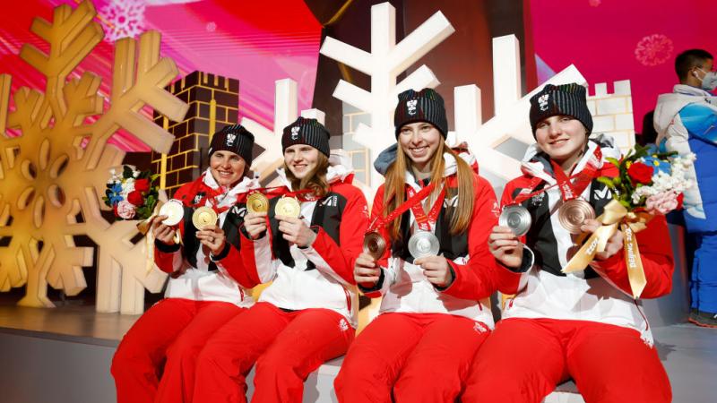 Four female athletes are posing for a photo while holding two medals each 