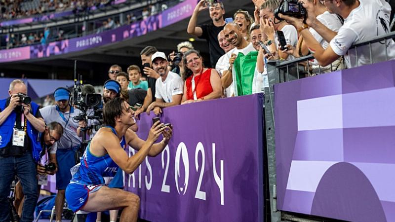 A man with a prosthetic leg kneeling to propose to his girlfriend in a packed stadium