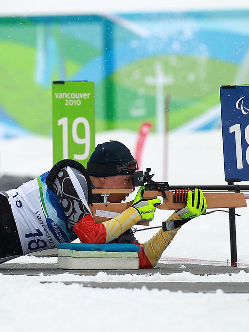 A female sit-skier is lying on the snow, aiming her rifle during a competition