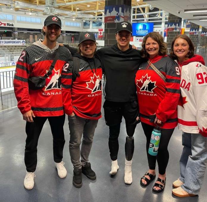 Five people wearing Canada's national red and white uniforms for Para ice hockey pose for a photo