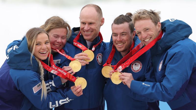 Five athletes pose for a photo while holding gold medals