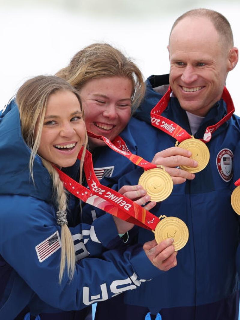 Five athletes pose for a photo while holding gold medals
