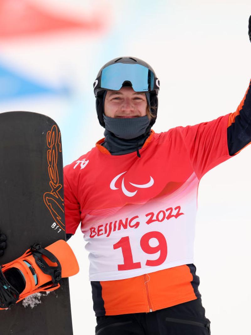 A male Para snowboard athlete posing for a photo while holding a snowboard