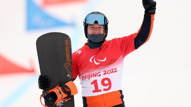 A male Para snowboard athlete posing for a photo while holding a snowboard