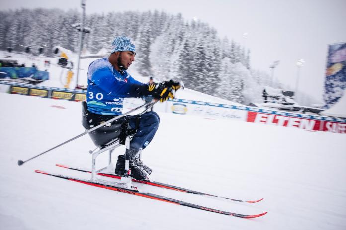A male Para athlete is competing in a Para cross-country skiing race in a sit-ski in the snow.