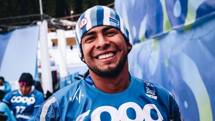 A male athlete wearing a blue beanie and a blue uniform is smiling
