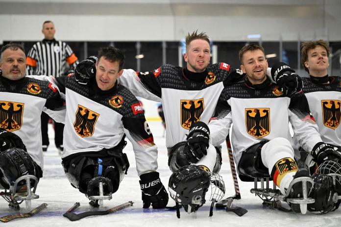 Five Para ice hockey athletes form a line on the ice, putting one's arm around their teammates' shoulder