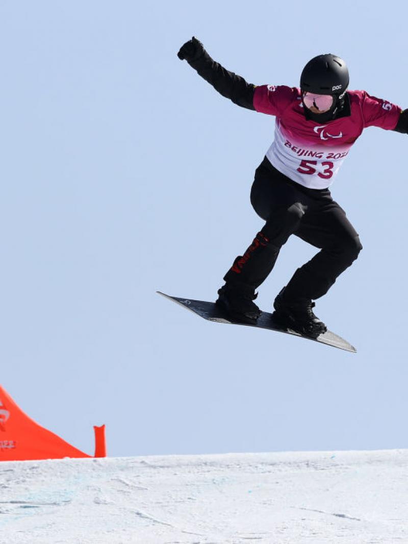 A man passing by a flag in a Para snowboard competition 