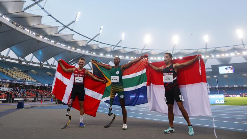 Three athletes with prosthetic legs with their country flags