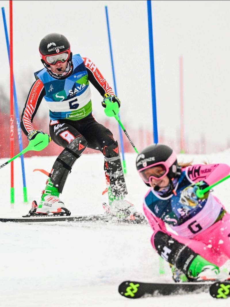 A male Para alpine skier is racing behind a female guide who is wearing a pink suit