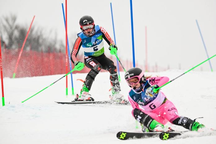 A male Para alpine skier is racing behind a female guide who is wearing a pink suit