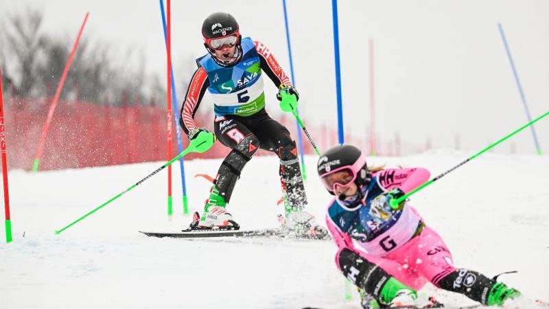 A male Para alpine skier is racing behind a female guide who is wearing a pink suit