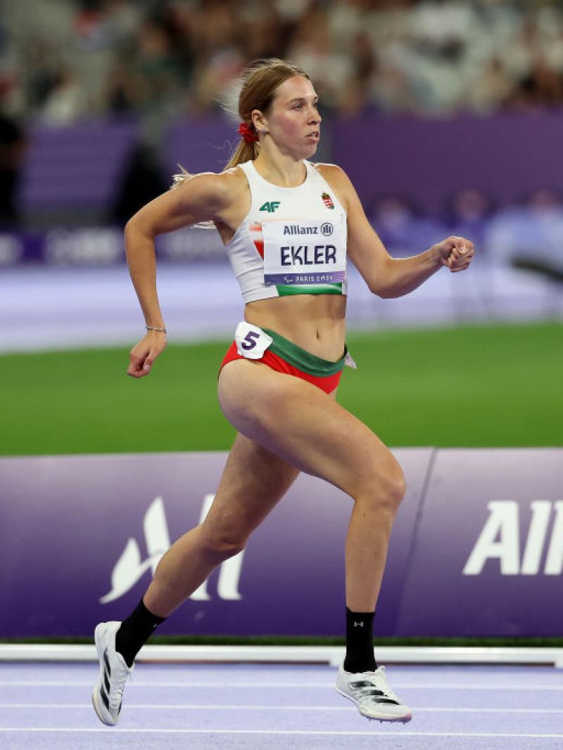 A female Paralympic sprinter competing at Paris 2024. Her bib has the logo of Allianz