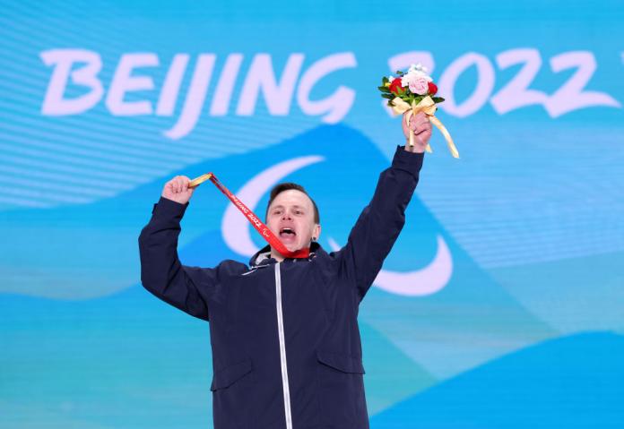 A male Para athlete celebrates on the podium with a gold medal