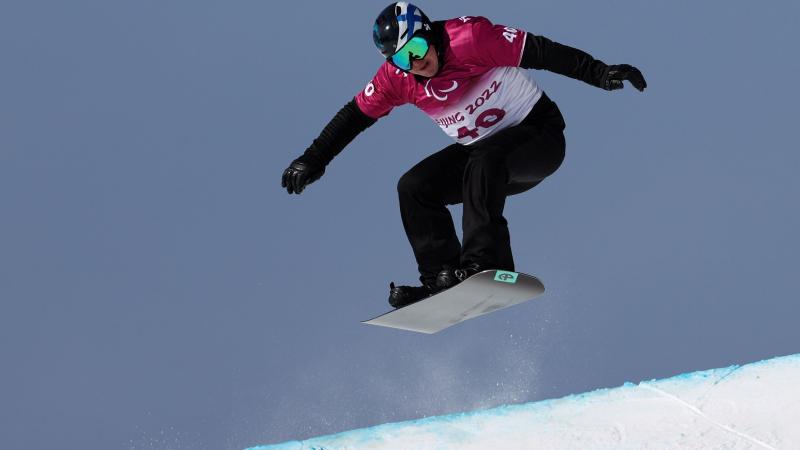 A male Para snowboarding athlete is in the air during a competition