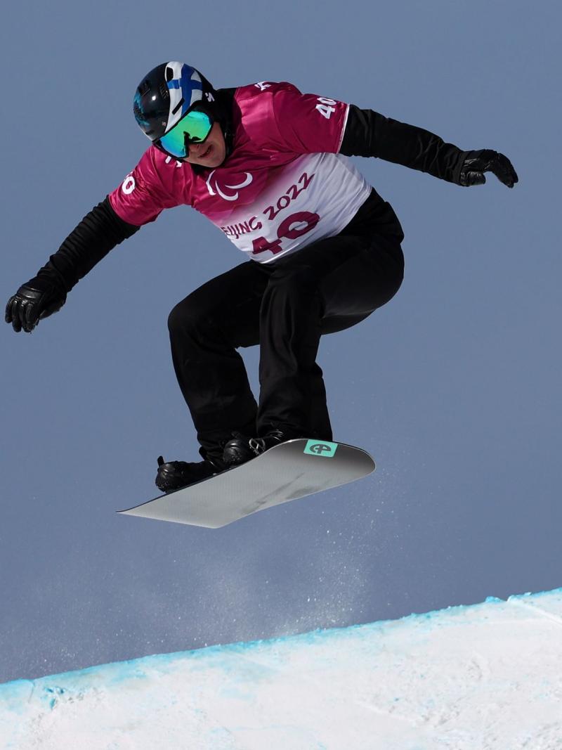 A male Para snowboarding athlete is in the air during a competition