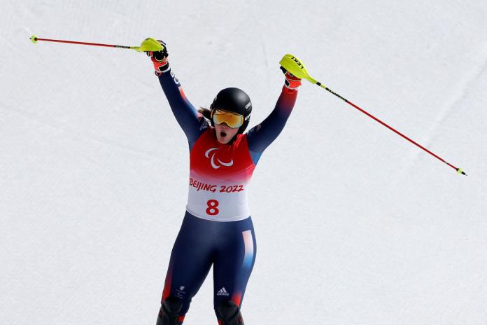 A female Para alpine skiing athlete raises her arms to celebrate