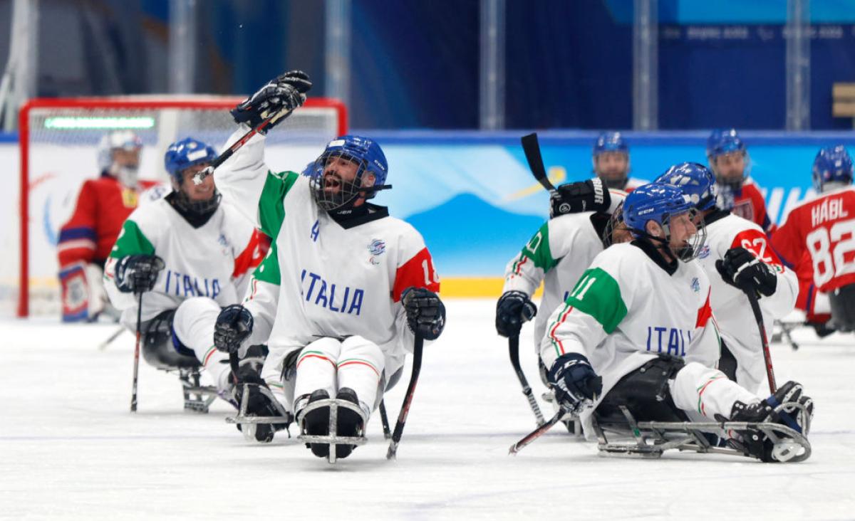 A male Para ice hockey player celebrates by raising his Para ice hockey stick on the ice