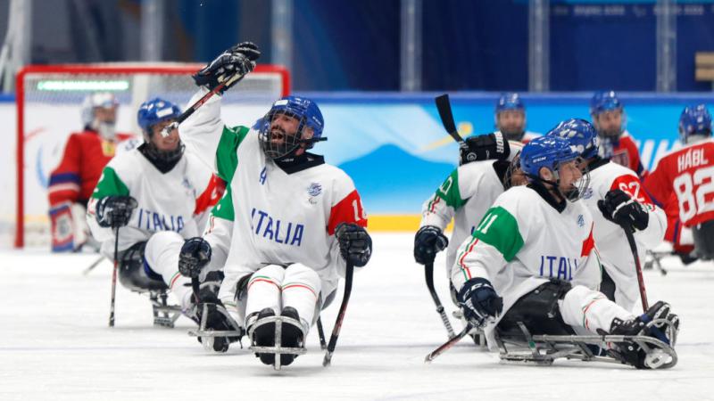 A male Para ice hockey player celebrates by raising his Para ice hockey stick on the ice