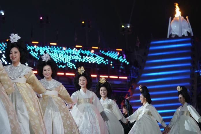 Female dancers dressed in Korea's traditional white dress are in a line in front of the PyeongChang 2018 cauldron