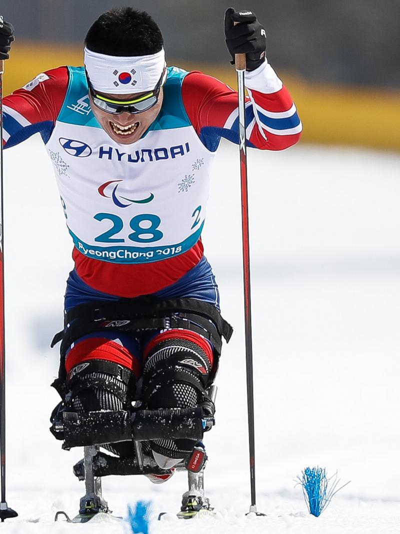 A man on sit ski's pushes himself towards the finish line with two sticks, one in each hand.