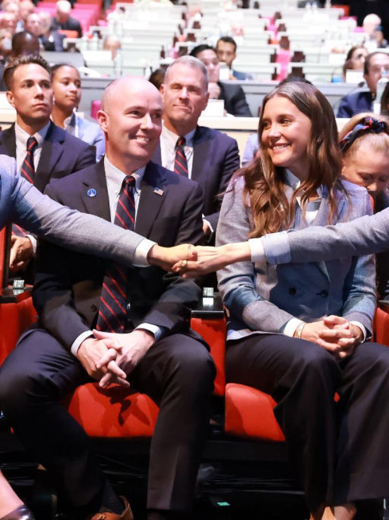 Four people sit side by side, with two of them holding each other's hands to celebrate