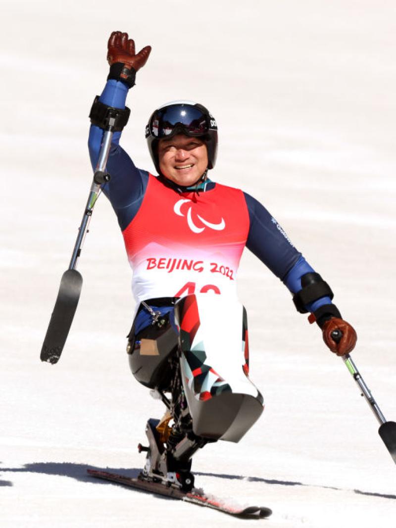 A male sit-skiing athlete is waving after a race