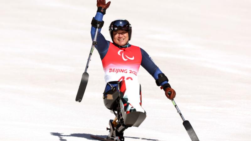 A male sit-skiing athlete is waving after a race