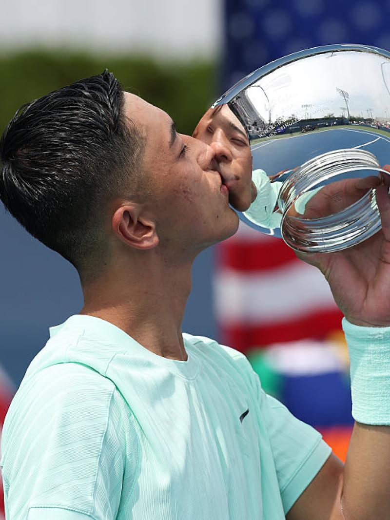 A male wheelchair tennis player is kissing a silver trophy
