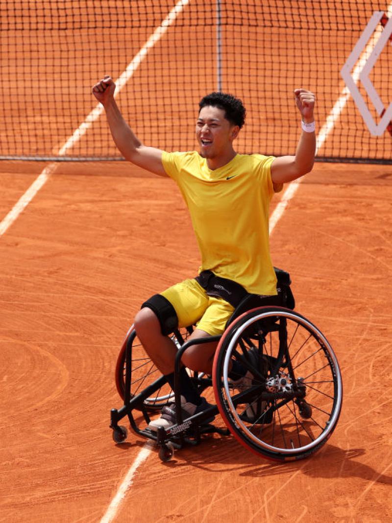A male wheelchair tennis player celebrates after winning match point on clay court