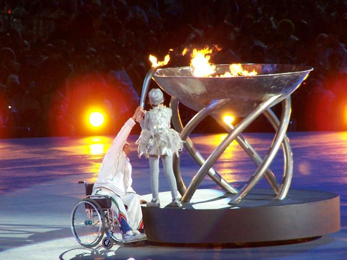 Two people are holding a torch together to light the cauldron of the Torino 2006 Paralympics