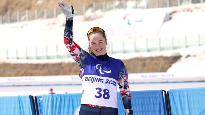 A female skiing athlete is waving after her race